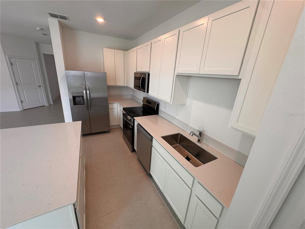 A modern kitchen features white cabinets, stainless steel appliances, and light-colored countertops — 3135 MINDFULLNESS DRIVE, CLERMONT, FL