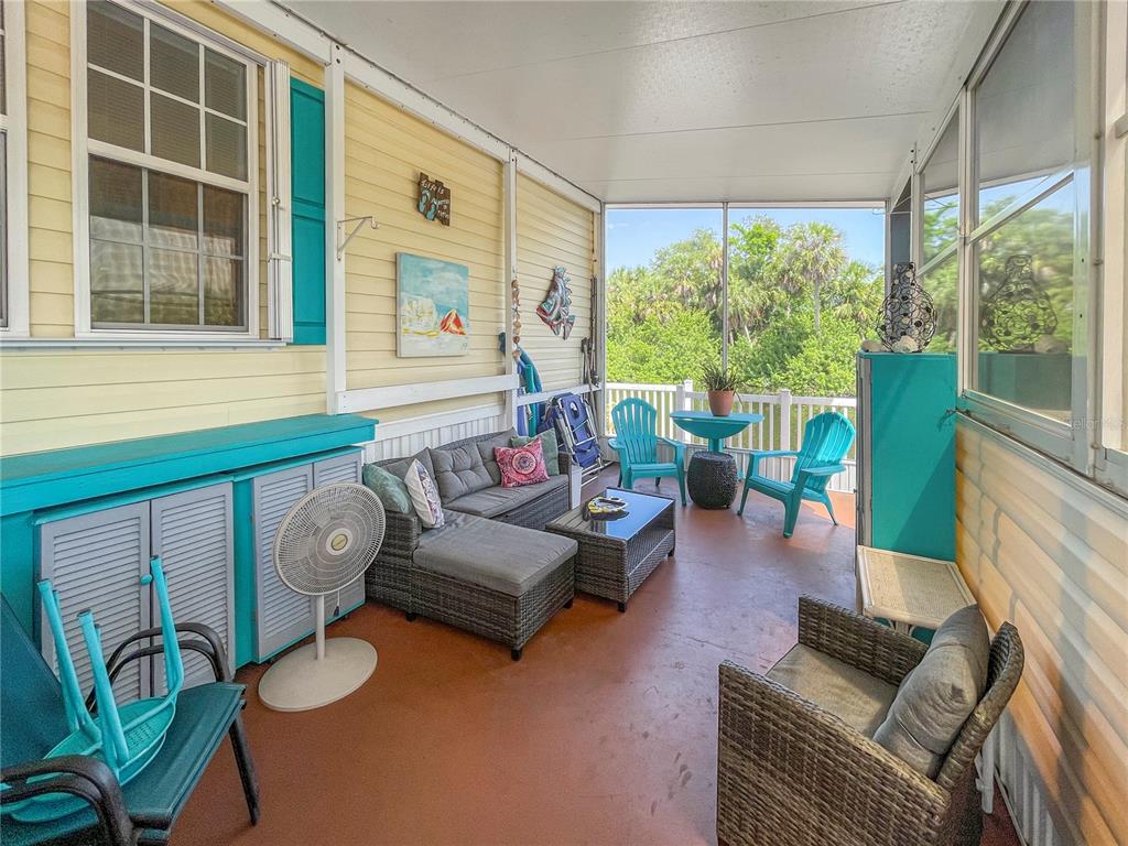 A screened-in porch features yellow siding, gray wicker furniture, and a view of trees — 10101 BURNT STORE ROAD UNIT 222, PUNTA GORDA, FL