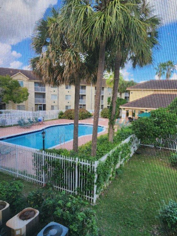 A view through a screen showing a swimming pool, palm trees, and apartment buildings — 460 S PARK # 209, Hollywood FL 33021, HOLLYWOOD, FL