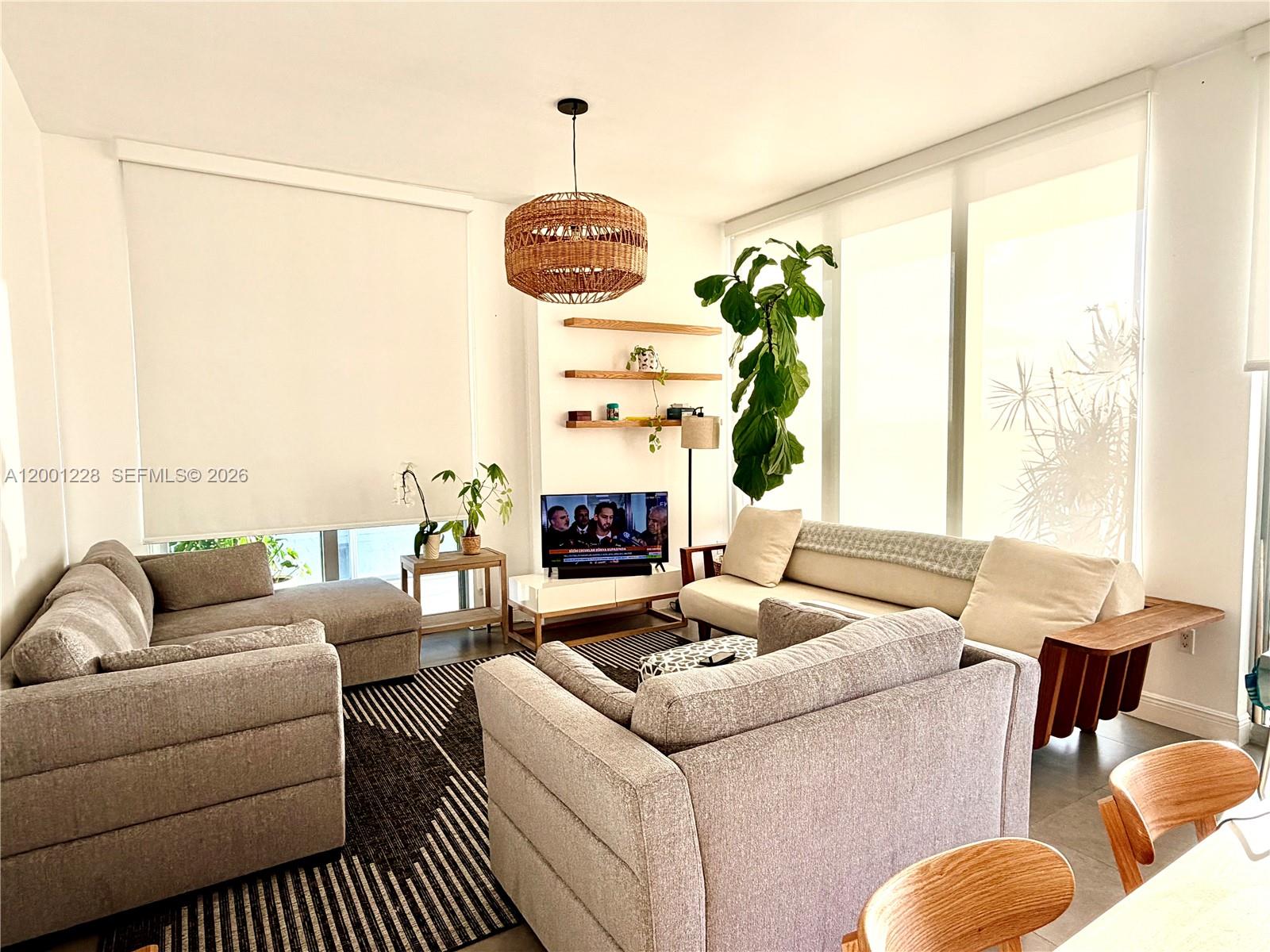 A living room features a sectional sofa, a television, floating shelves, and large windows — 3470 E Coast Ave # H1610, Miami FL 33137, MIAMI, FL