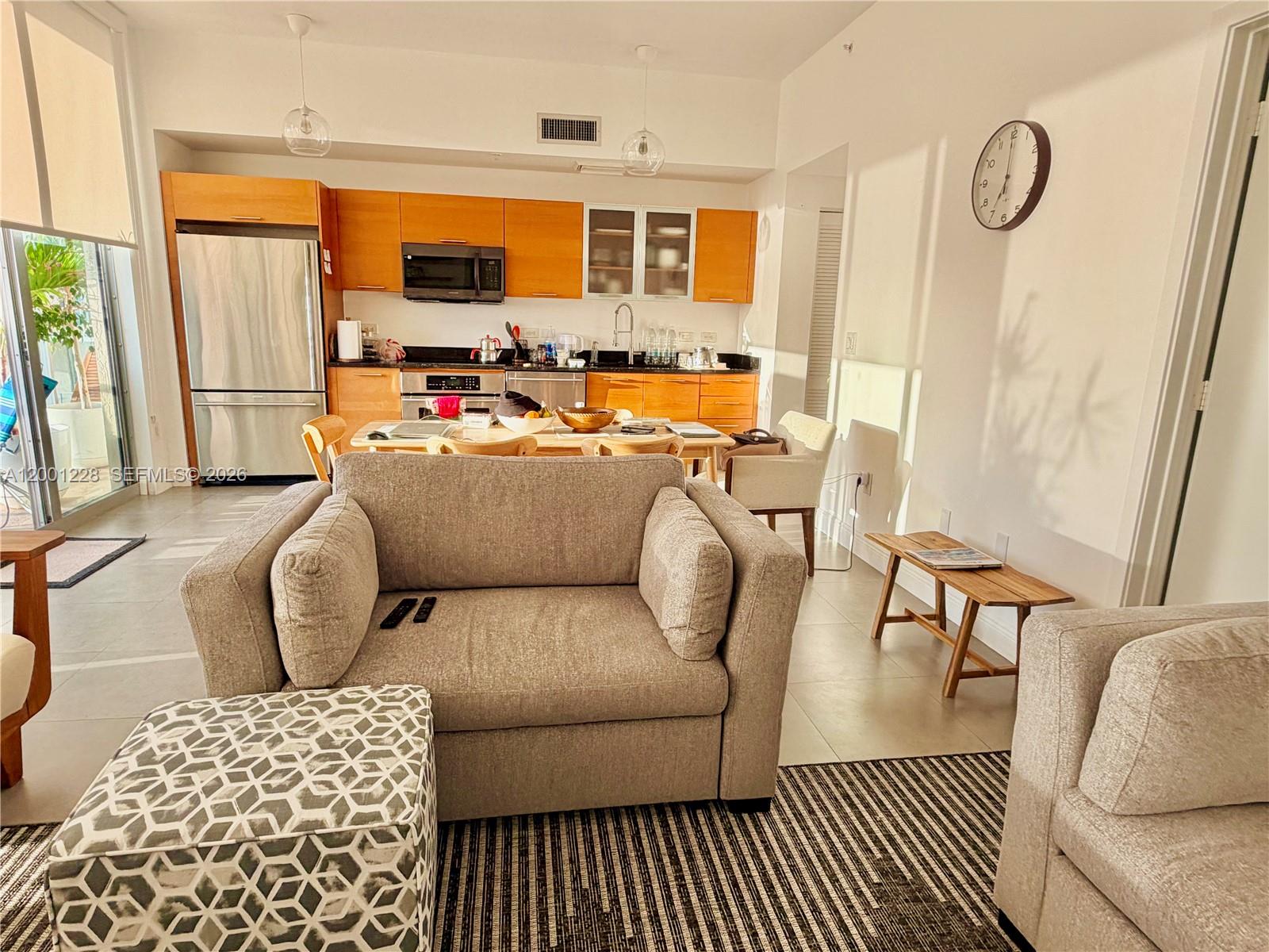 A living room with a beige sofa and patterned ottoman opens to a kitchen area — 3470 E Coast Ave # H1610, Miami FL 33137, MIAMI, FL