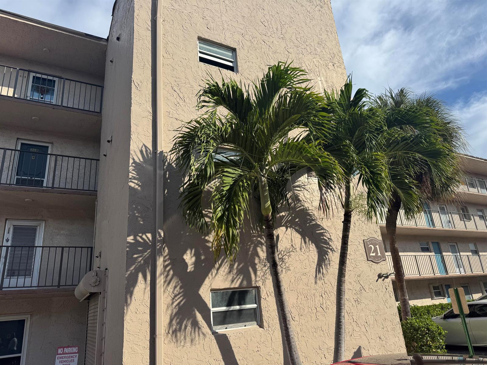 Exterior view of a beige stucco apartment building labeled Building 21 with palm trees — 725 Lori Drive # 107, Palm Springs FL 33461, PALM SPRINGS, FL