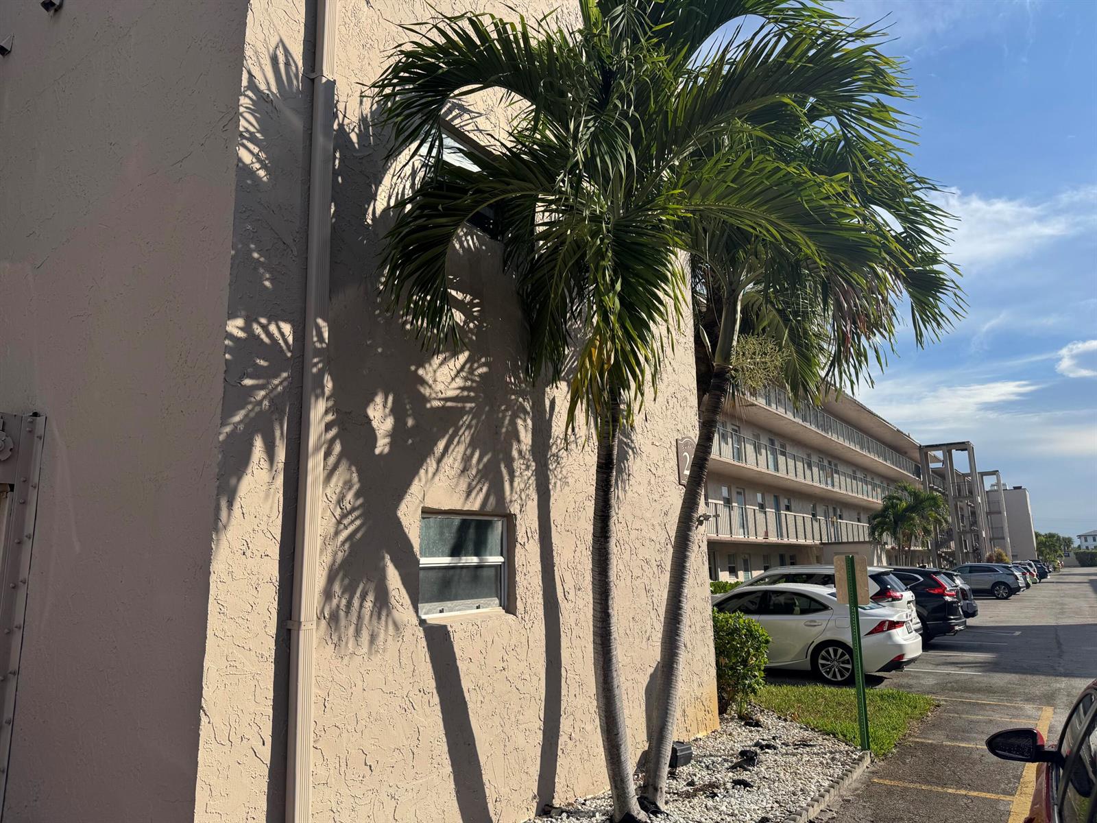Exterior view of a multi-story apartment building with palm trees and parked cars — 725 Lori Drive # 107, Palm Springs FL 33461, PALM SPRINGS, FL