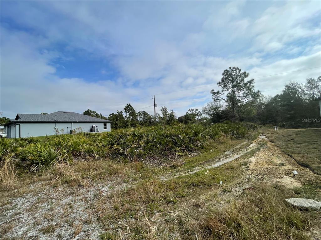A vacant, grassy lot with palmetto bushes sits next to a single-story residential home — 150 CHICKERING STREET, PORT CHARLOTTE, FL