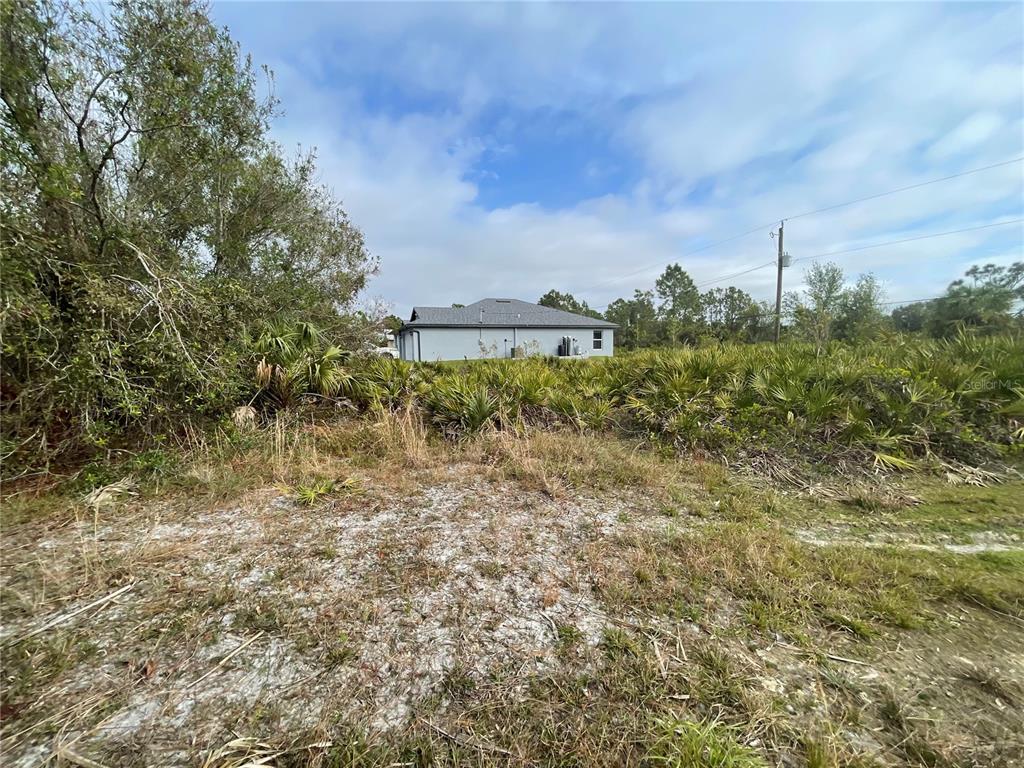 A vacant, sandy lot with low-lying vegetation sits in front of a single-story house — 150 CHICKERING STREET, PORT CHARLOTTE, FL