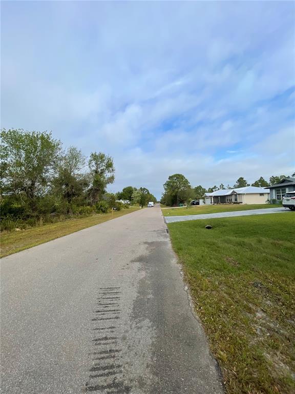 A paved residential street stretches into the distance past grassy lots and suburban houses — 150 CHICKERING STREET, PORT CHARLOTTE, FL