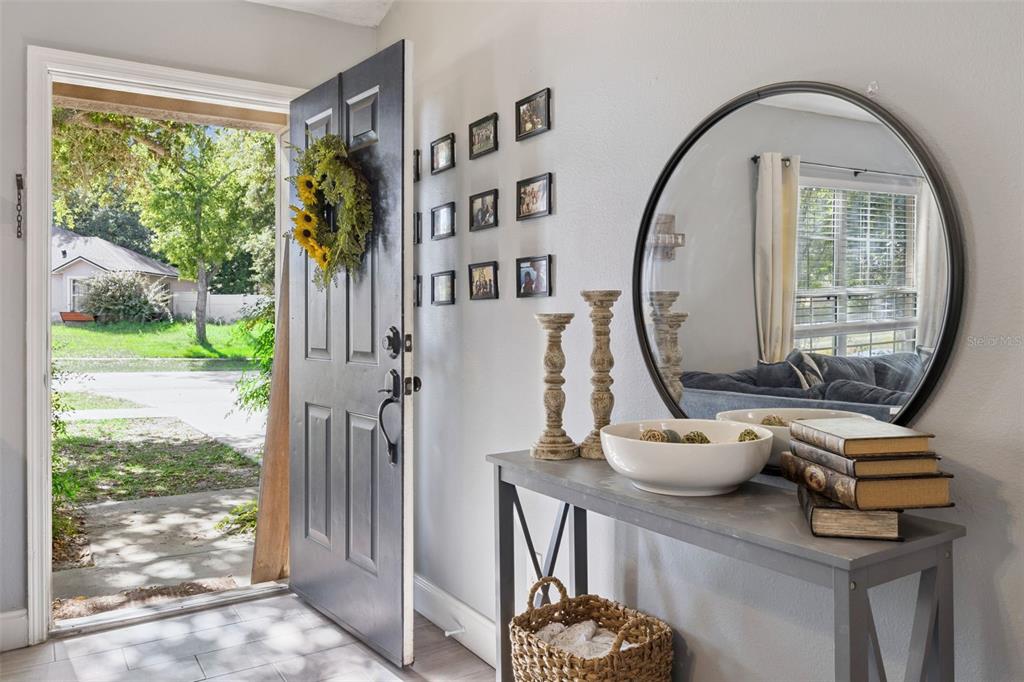 An entryway features a gray console table, a round mirror, and an open front door — 648 TRANQUILITY STREET, MINNEOLA, FL