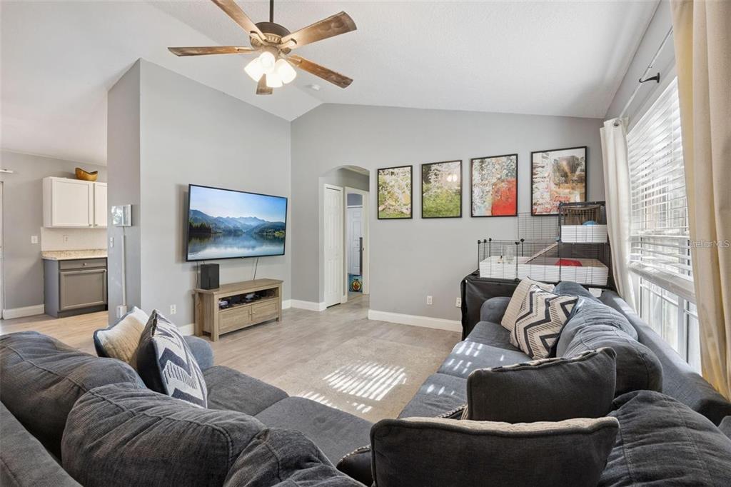 A living room features a gray sectional sofa, a wall-mounted television, and light wood flooring — 648 TRANQUILITY STREET, MINNEOLA, FL