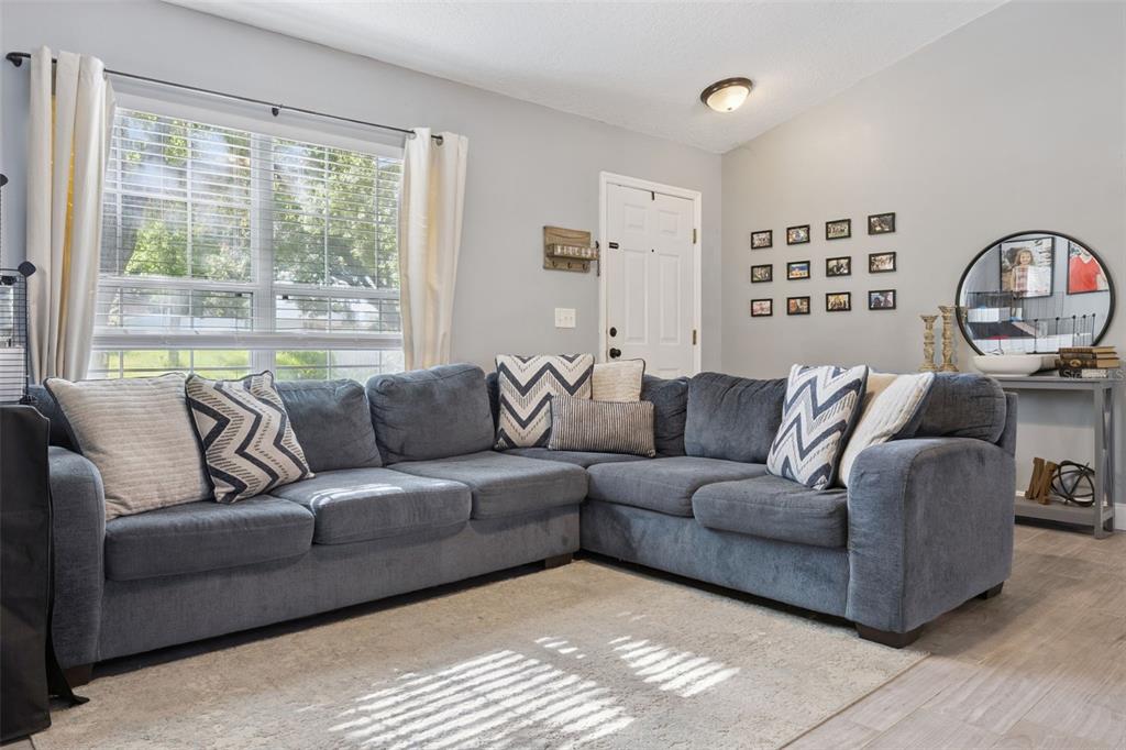 A living room features a large gray sectional sofa, a light rug, and a window — 648 TRANQUILITY STREET, MINNEOLA, FL
