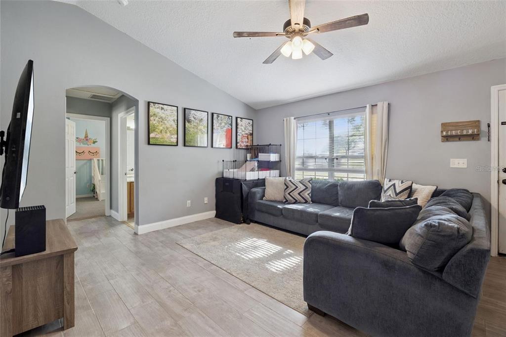 A living room features gray walls, wood-look flooring, a sectional sofa, and a ceiling fan — 648 TRANQUILITY STREET, MINNEOLA, FL