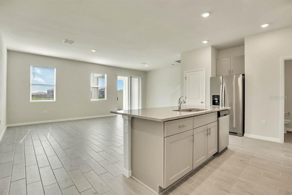 A kitchen with a central island and stainless steel appliances opens into a living area — 1758 WOODLEAF HAMMOCK COURT, BRADENTON, FL