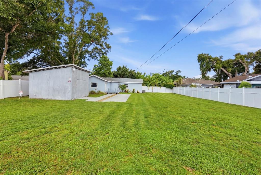 A large backyard features a metal shed, a concrete patio, and a white vinyl fence — 4978 71ST STREET N, ST PETERSBURG, FL