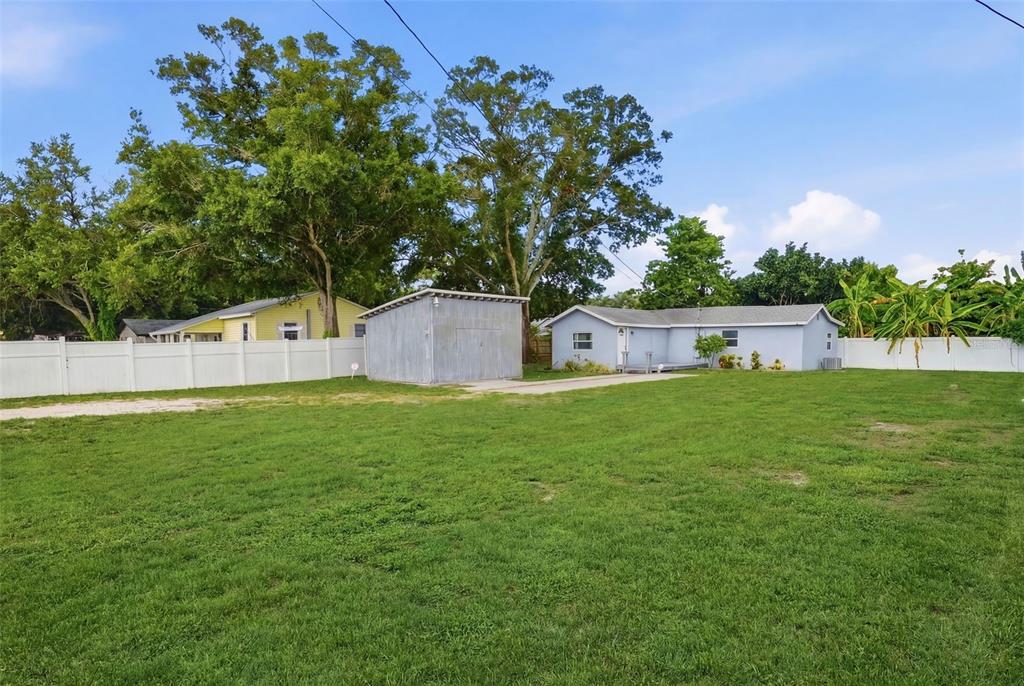 A large grassy backyard features a detached metal shed and a light blue house — 4978 71ST STREET N, ST PETERSBURG, FL
