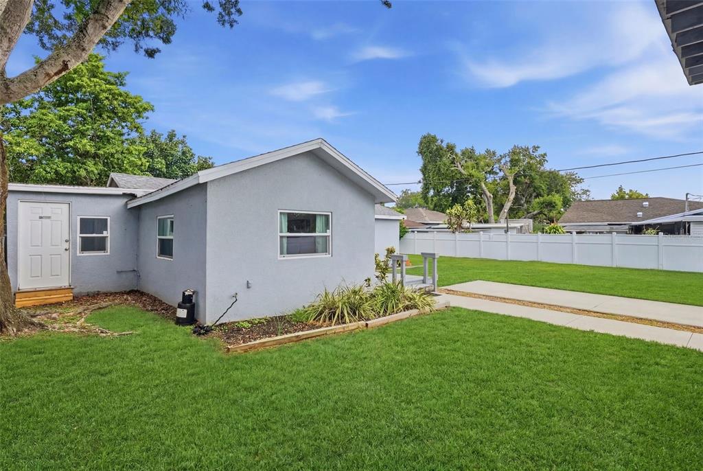 A light gray house exterior features a white door, windows, and a grassy backyard — 4978 71ST STREET N, ST PETERSBURG, FL