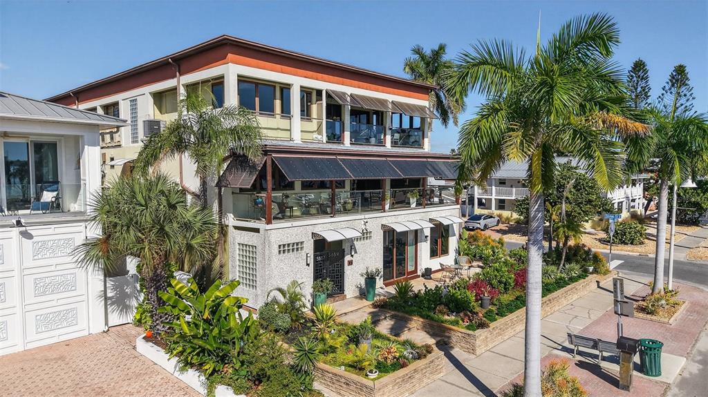 An exterior view of a multi-story building with balconies, palm trees, and a landscaped garden — 5659 SHORE BOULEVARD S, GULFPORT, FL