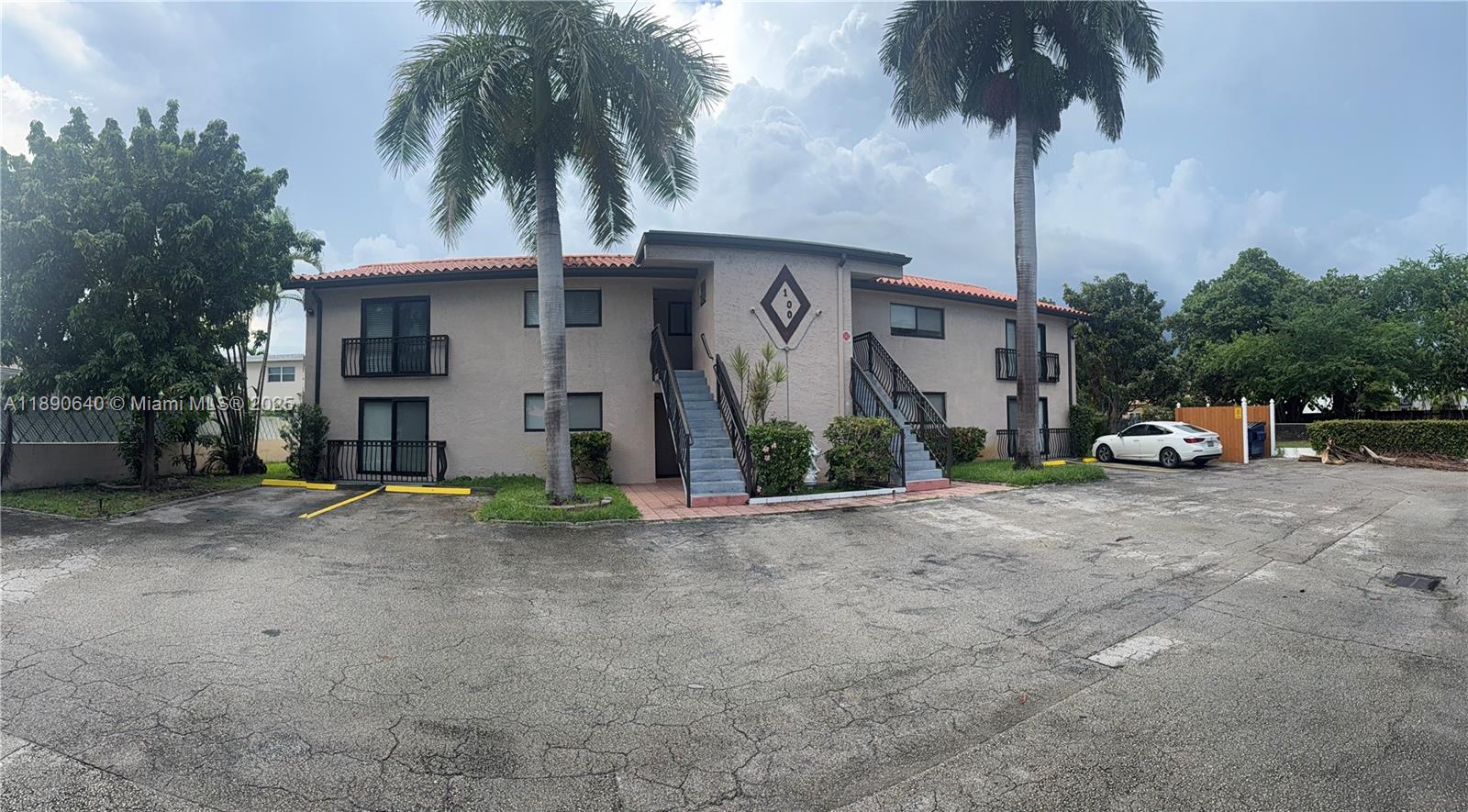 A two-story apartment building features a tan exterior, two staircases, and palm trees — 100 SE 5th Ave # 1, Hallandale Beach FL 33009, HALLANDALE BEACH, FL