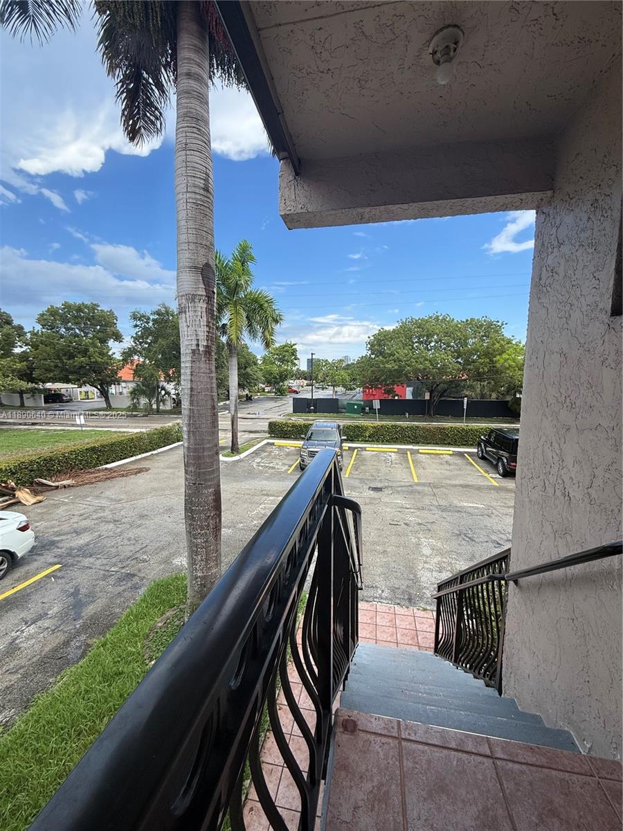 An outdoor staircase with a black metal railing overlooks a parking lot and trees — 100 SE 5th Ave # 1, Hallandale Beach FL 33009, HALLANDALE BEACH, FL