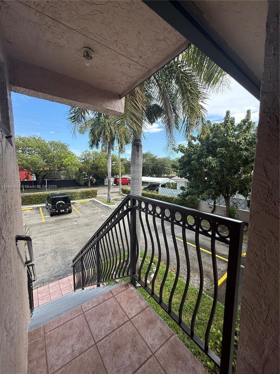 An outdoor staircase with a black metal railing overlooks a parking lot and palm trees — 100 SE 5th Ave # 1, Hallandale Beach FL 33009, HALLANDALE BEACH, FL
