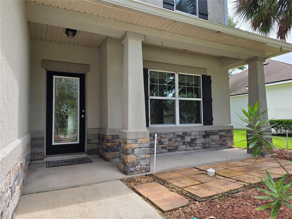 The front exterior of a house features a covered porch, stone veneer, and a glass-paneled door — 404 PAISLEY PLACE, ST JOHNS, FL