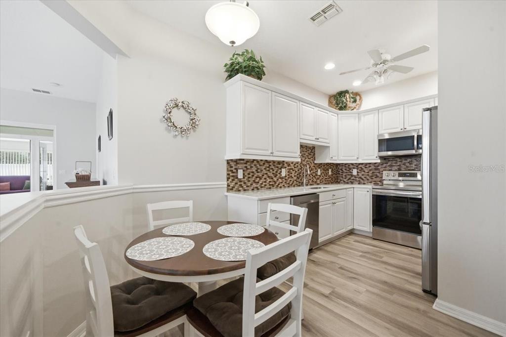 A kitchen with white cabinets, a mosaic tile backsplash, and a small round dining table — 15028 SILVERSMITH CIRCLE, SPRING HILL, FL