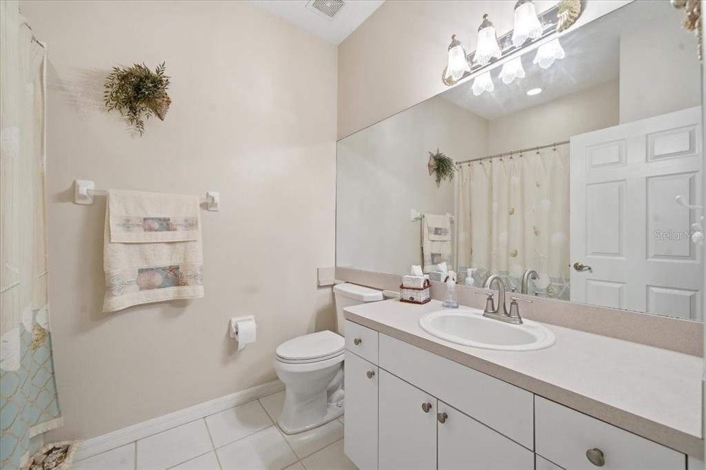 A bathroom features white cabinets, a single vanity sink, a toilet, and a large mirror — 15028 SILVERSMITH CIRCLE, SPRING HILL, FL