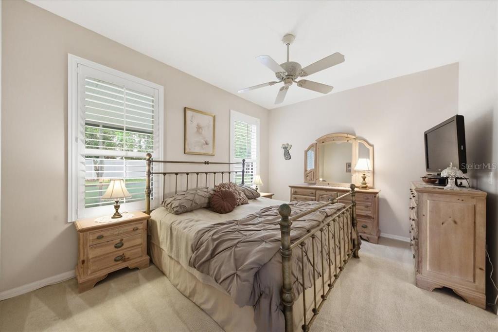 A bedroom features a metal bed frame, wooden furniture, and two windows with white shutters — 15028 SILVERSMITH CIRCLE, SPRING HILL, FL