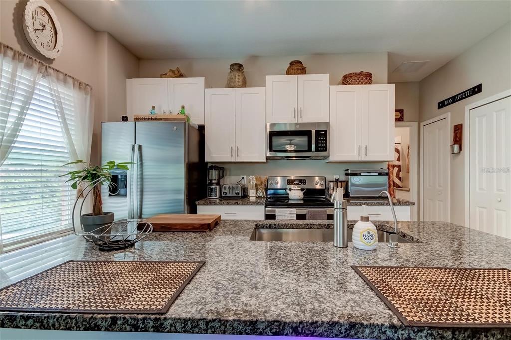 A kitchen features white cabinets, stainless steel appliances, and a granite-topped island with a sink — 4626 WILLET COOPER COURT, TAMPA, FL