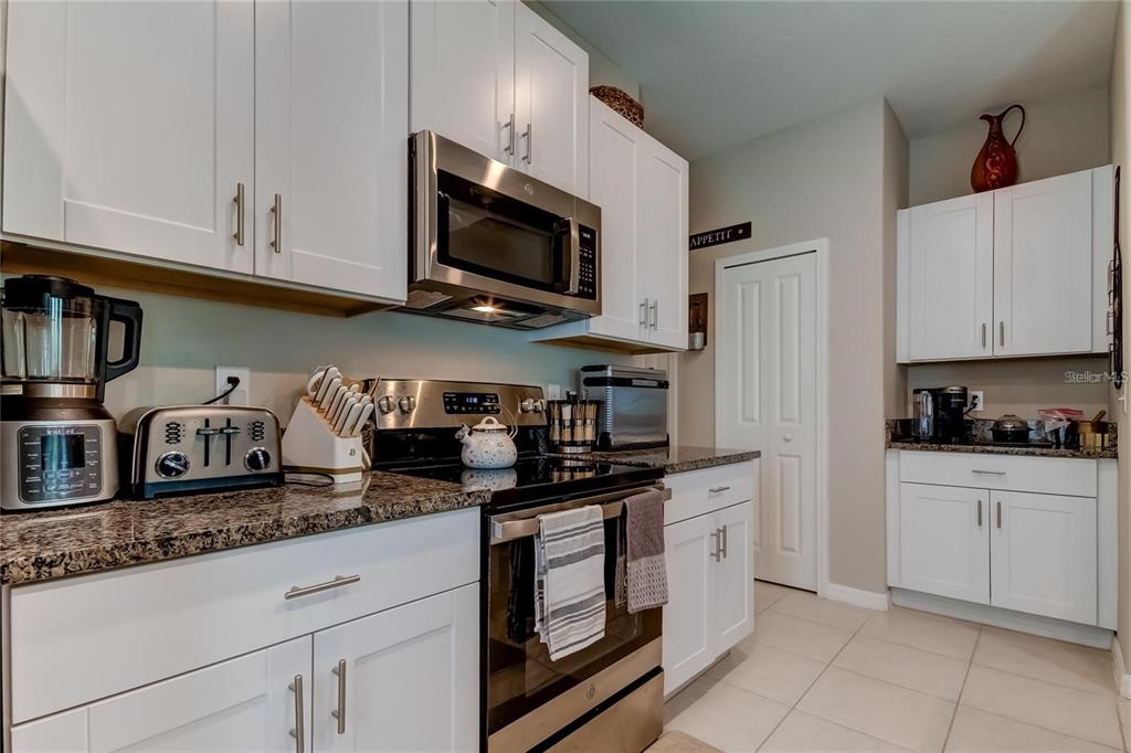 A kitchen features white cabinets, granite countertops, stainless steel appliances, and light-colored tile flooring — 4626 WILLET COOPER COURT, TAMPA, FL