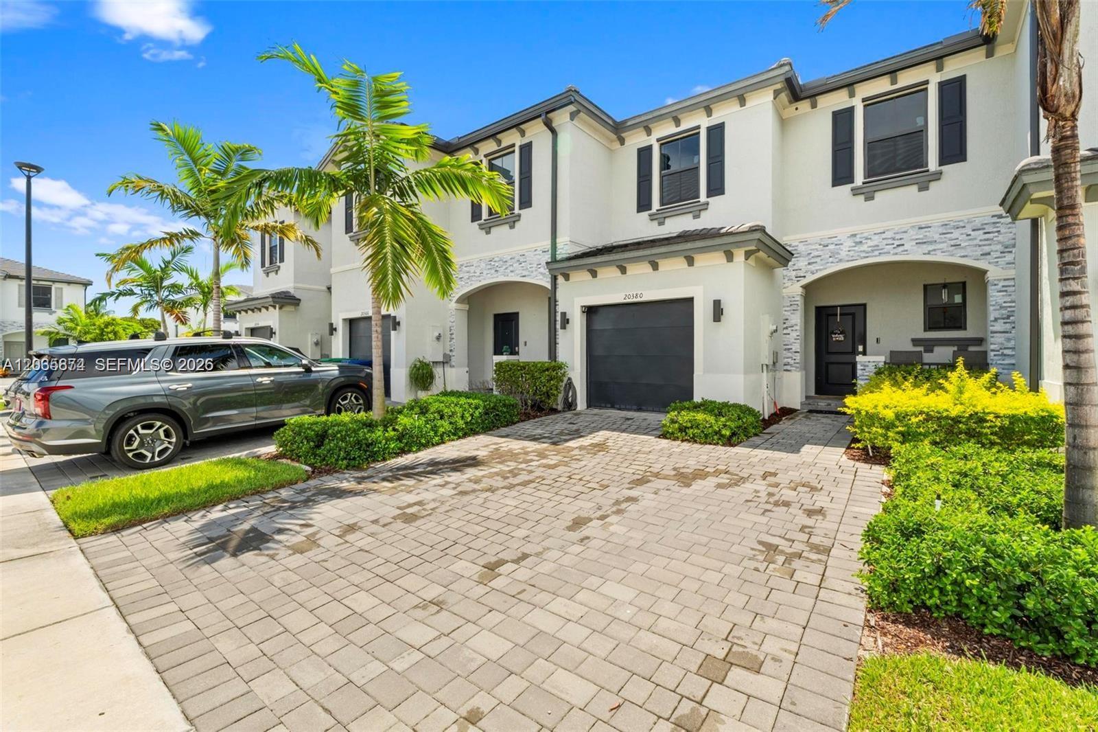 A two-story townhouse with a paved driveway, a one-car garage, and palm trees — 20380 NW 5th Ct, Miami Gardens FL 33169, MIAMI GARDENS, FL