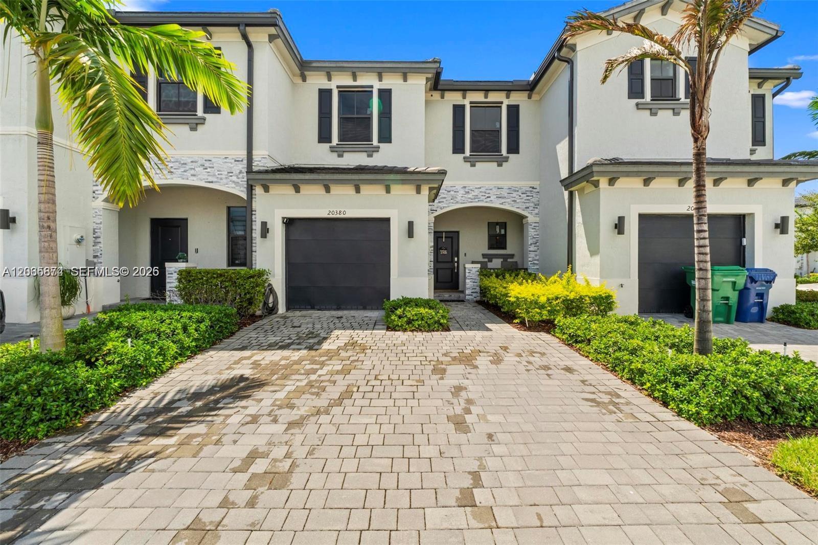 A two-story townhouse exterior features a paved driveway, dark garage doors, and palm trees — 20380 NW 5th Ct, Miami Gardens FL 33169, MIAMI GARDENS, FL
