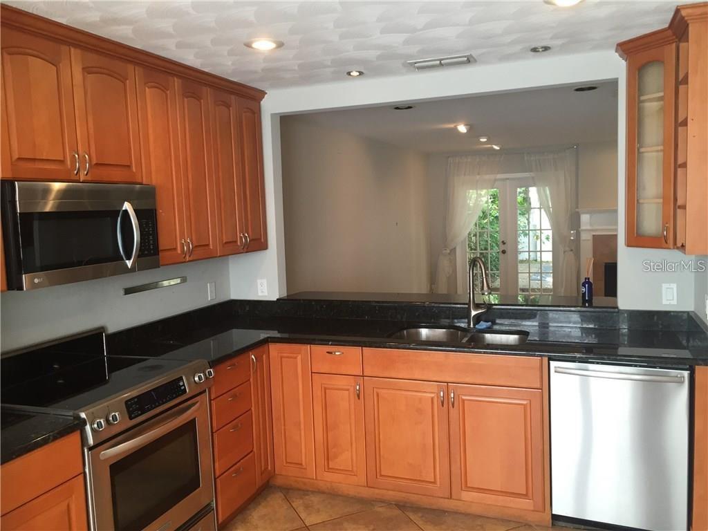 A kitchen with wood cabinets, black countertops, stainless steel appliances, and a pass-through window — 5300 BAYSHORE BOULEVARD UNIT A5, TAMPA, FL