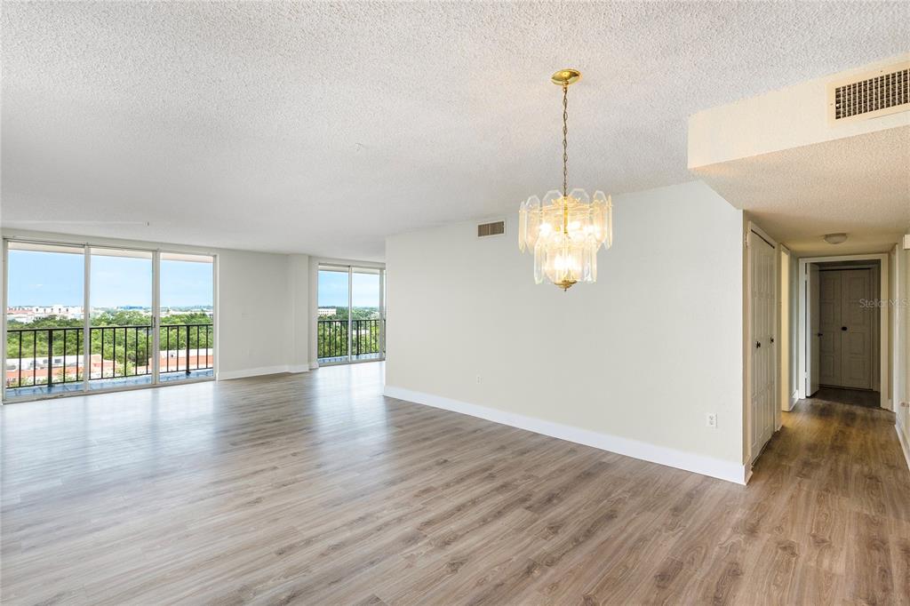 An empty living area features light wood-look flooring, a crystal chandelier, and floor-to-ceiling windows — 2699 SEVILLE BOULEVARD UNIT 802, CLEARWATER, FL