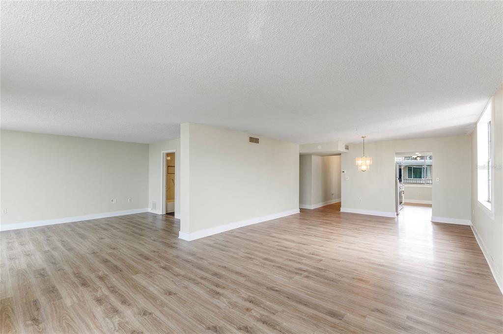 An empty living area with light wood-look flooring, white walls, and a ceiling light fixture — 2699 SEVILLE BOULEVARD UNIT 802, CLEARWATER, FL