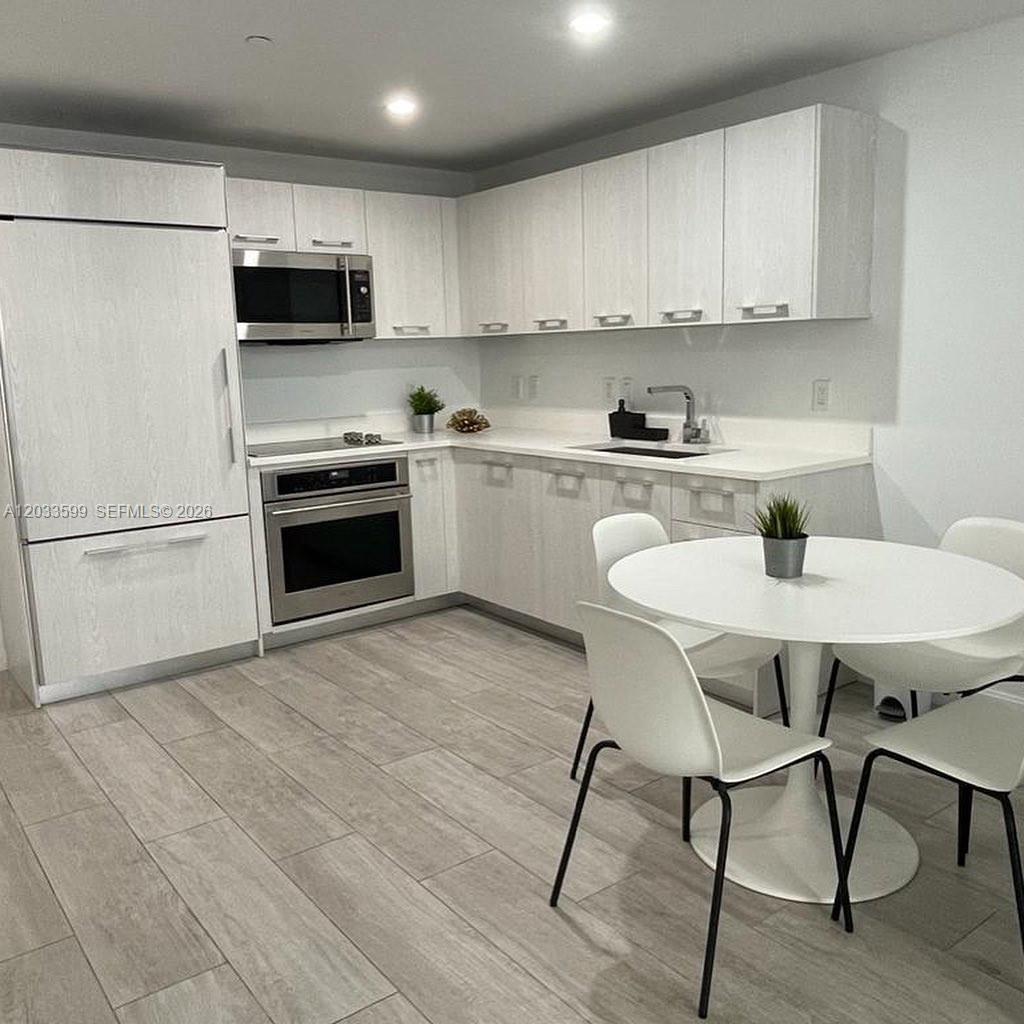 A modern kitchen features light wood-grain cabinets, stainless steel appliances, and a white dining set — 45 SW 9th St # 1407, Miami FL 33130, MIAMI, FL