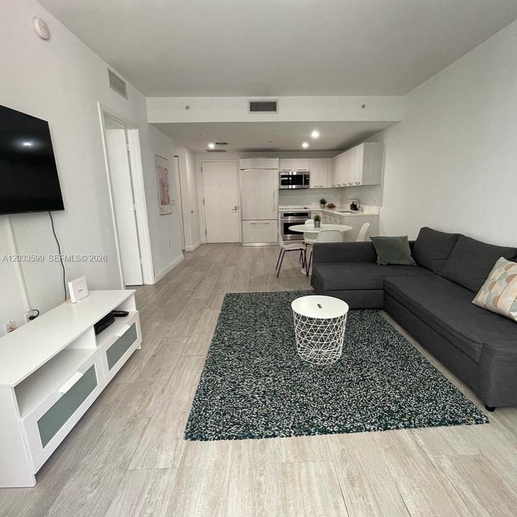 This open-concept living area features a gray sectional sofa, a white media console, and kitchen — 45 SW 9th St # 1407, Miami FL 33130, MIAMI, FL