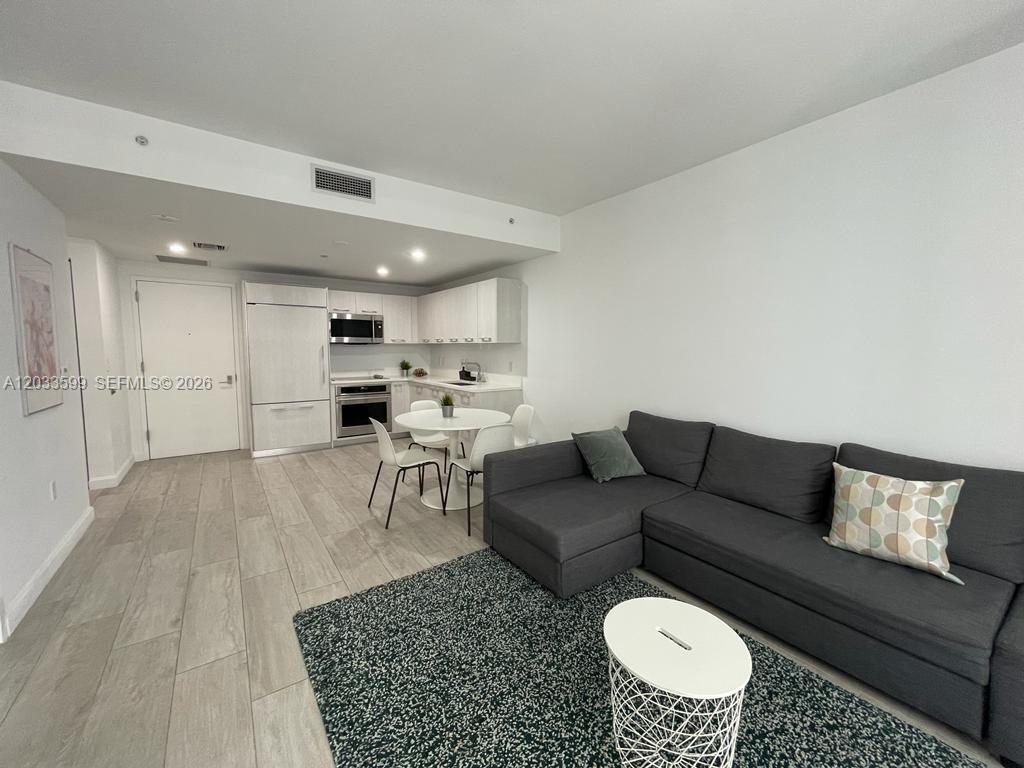 A modern open-concept living area features a kitchen, dining table, and a gray sectional sofa — 45 SW 9th St # 1407, Miami FL 33130, MIAMI, FL