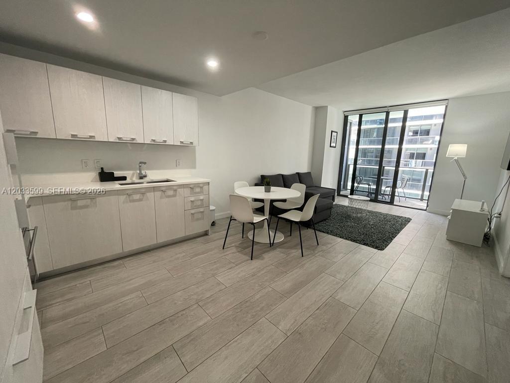 A modern open-concept kitchen and living area features light wood cabinetry and tile flooring — 45 SW 9th St # 1407, Miami FL 33130, MIAMI, FL