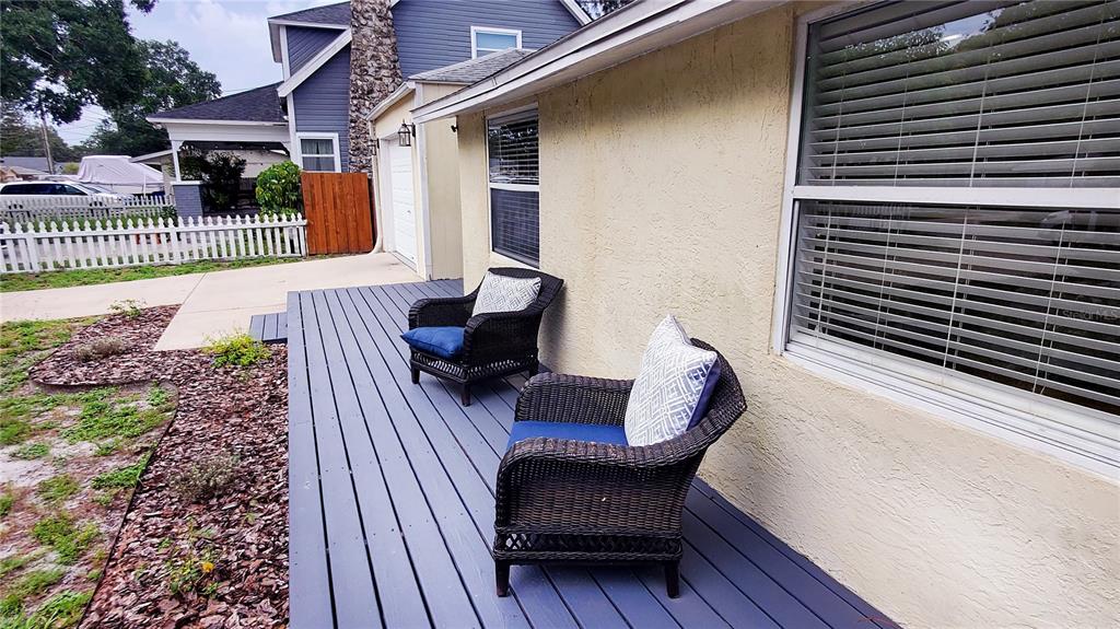 Two wicker chairs with blue cushions sit on a gray wooden deck beside a house — 1722 ALBEMARLE ROAD, CLEARWATER, FL