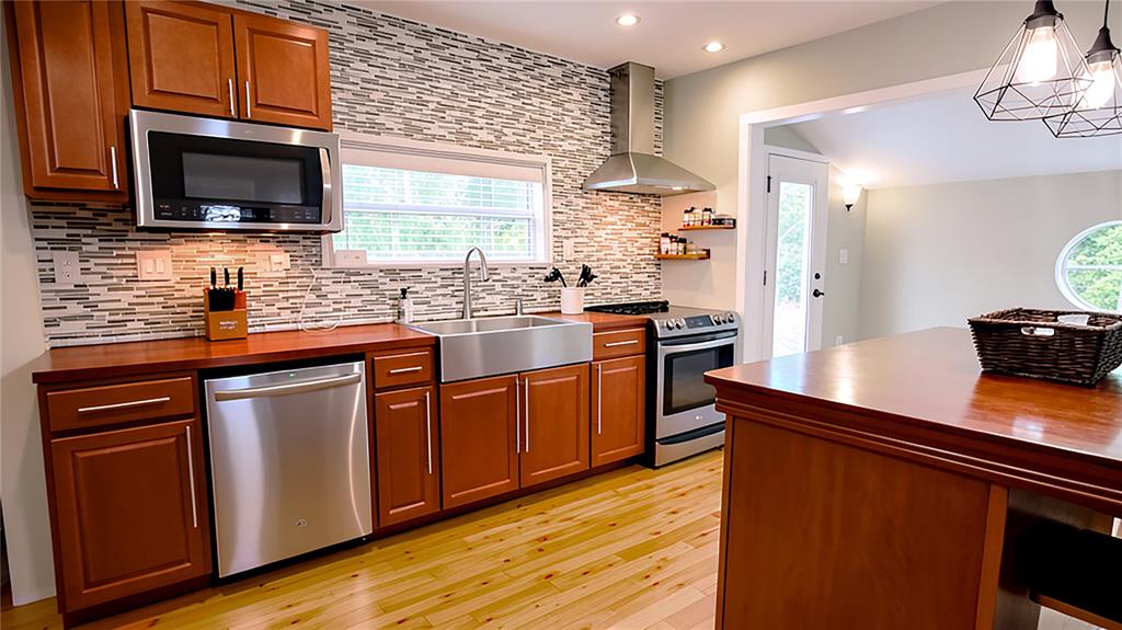 A kitchen features wood cabinets, stainless steel appliances, a farmhouse sink, and a tiled backsplash — 1722 ALBEMARLE ROAD, CLEARWATER, FL