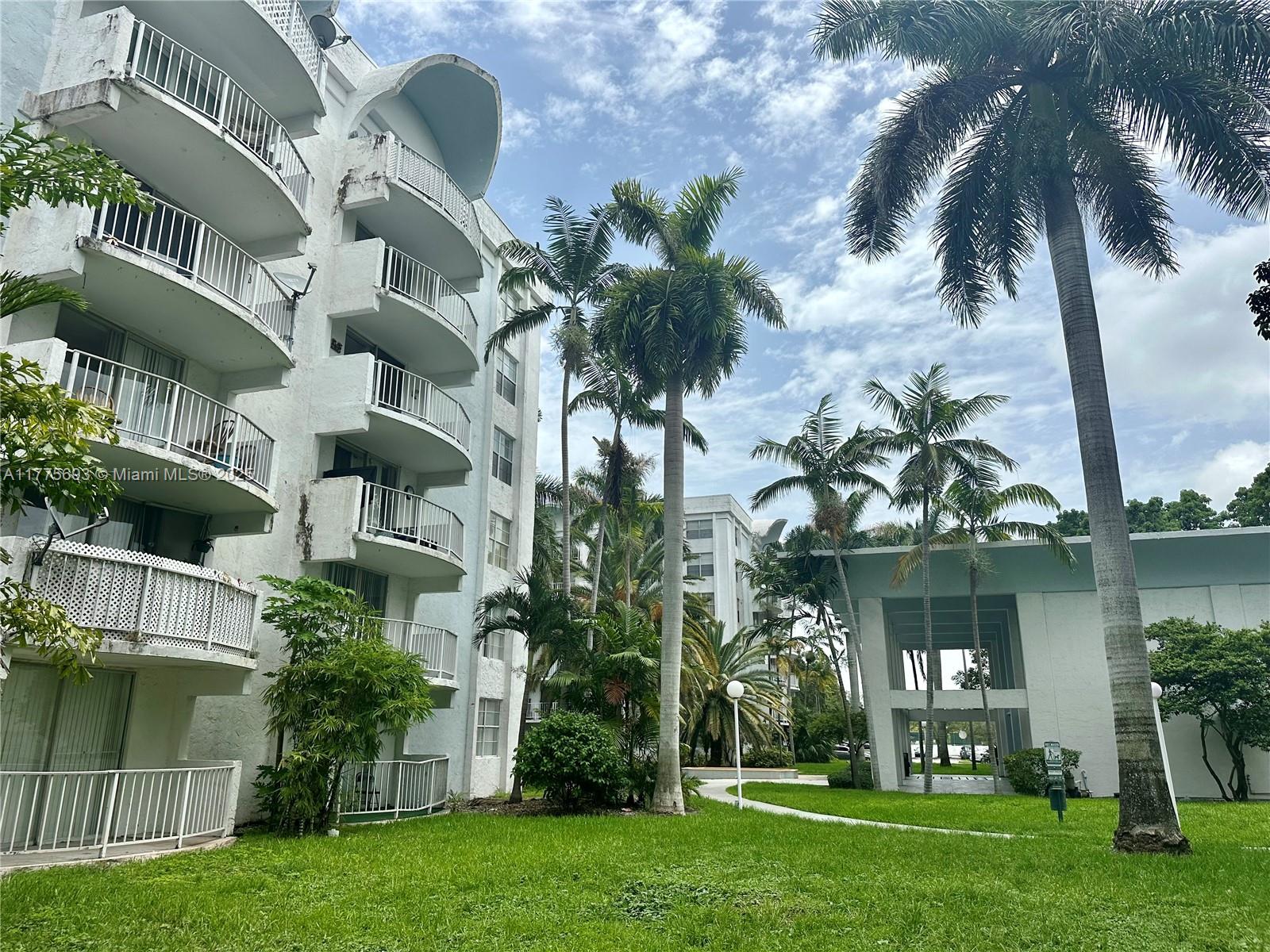 A multi-story white apartment building stands beside a grassy courtyard with several palm trees — 484 NW 165th St Rd # 316, Miami FL 33169, MIAMI, FL