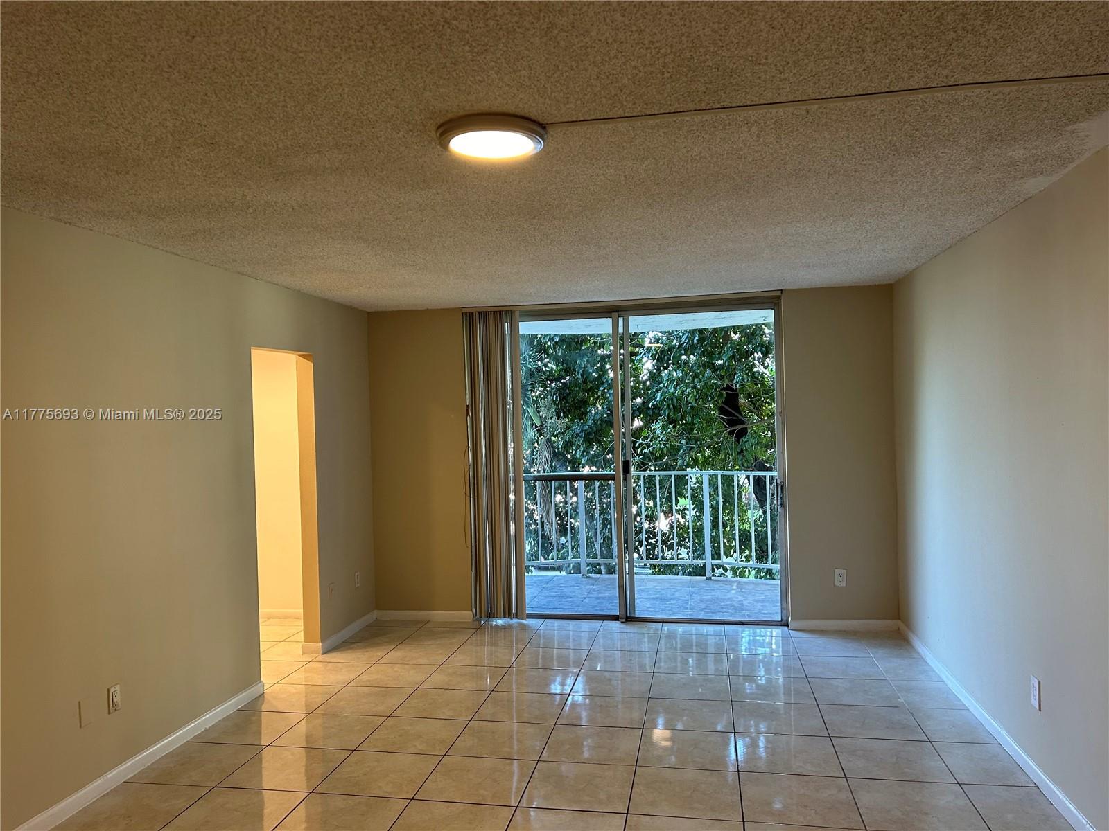 An empty room features beige tile floors, a textured ceiling, and a sliding glass door — 484 NW 165th St Rd # 316, Miami FL 33169, MIAMI, FL