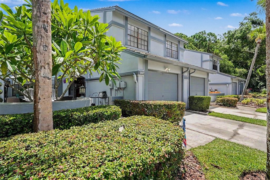 A two-story townhouse with a gray garage, light-colored siding, and a manicured hedge in front — 4107 BRENTWOOD PARK CIRCLE, TAMPA, FL