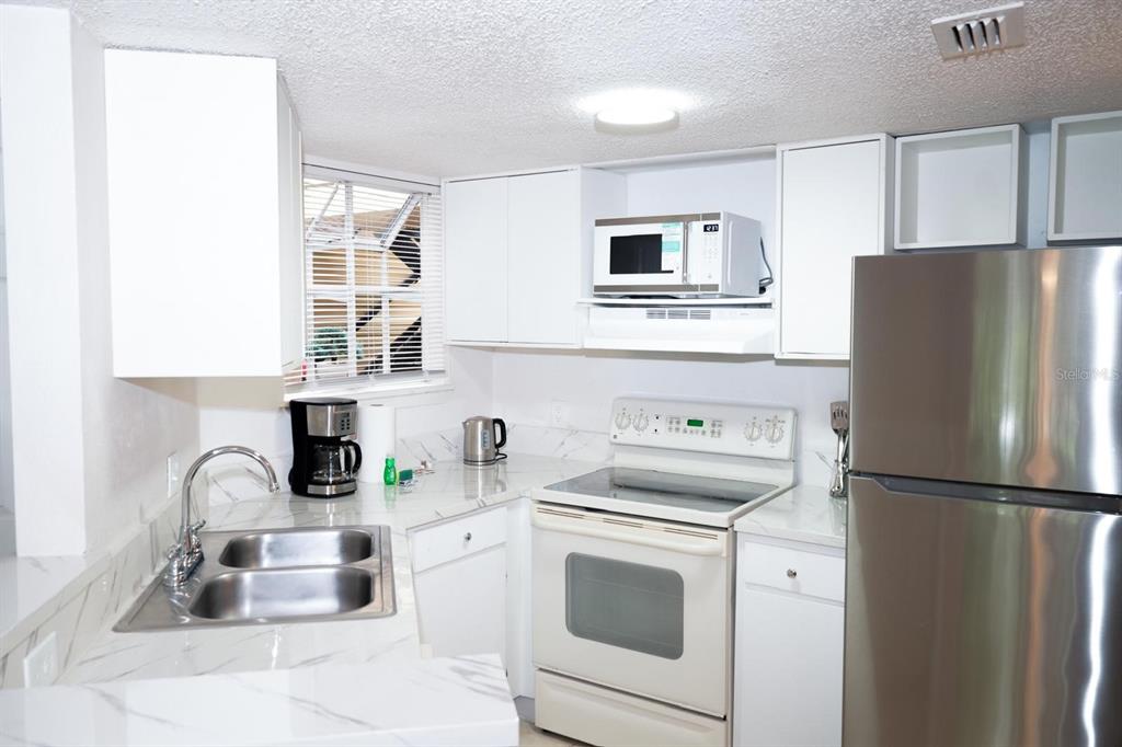 A kitchen features white cabinets, marble-look countertops, a stainless steel refrigerator, and a white stove — 1916 LAKE ATRIUMS CIRCLE UNIT 44, ORLANDO, FL