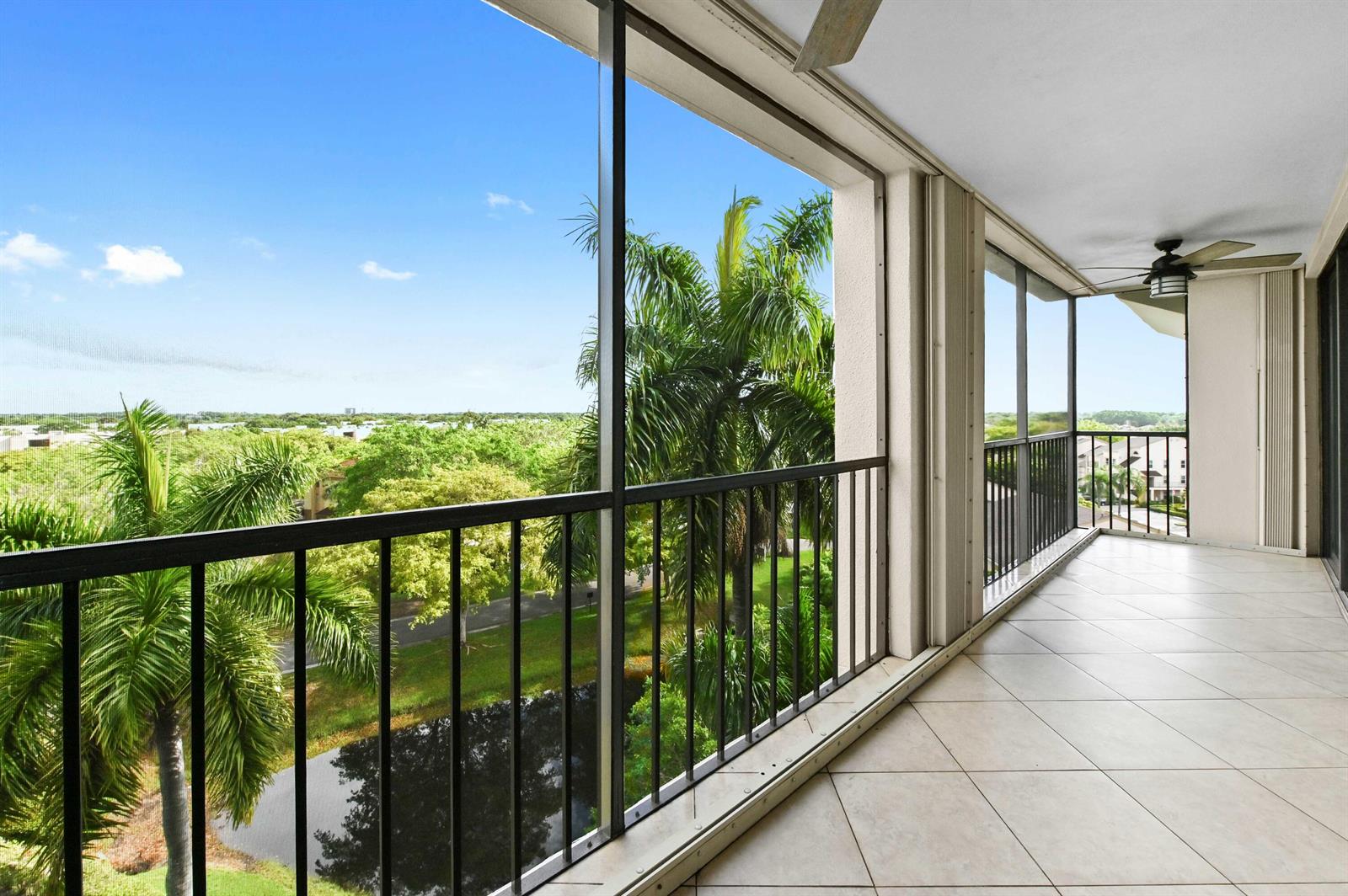 A screened-in balcony with tiled flooring, a ceiling fan, and views of trees and water — 5951 Wellesley Park Drive Apt 702, Boca Raton FL 33433, BOCA RATON, FL