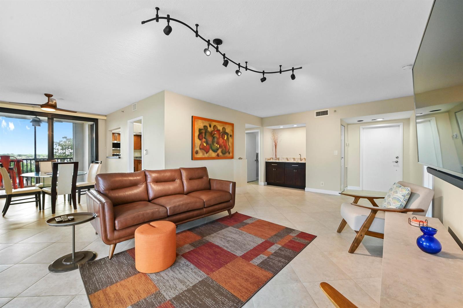 A living room features a brown leather sofa, a patterned rug, and a wet bar — 5951 Wellesley Park Drive Apt 702, Boca Raton FL 33433, BOCA RATON, FL