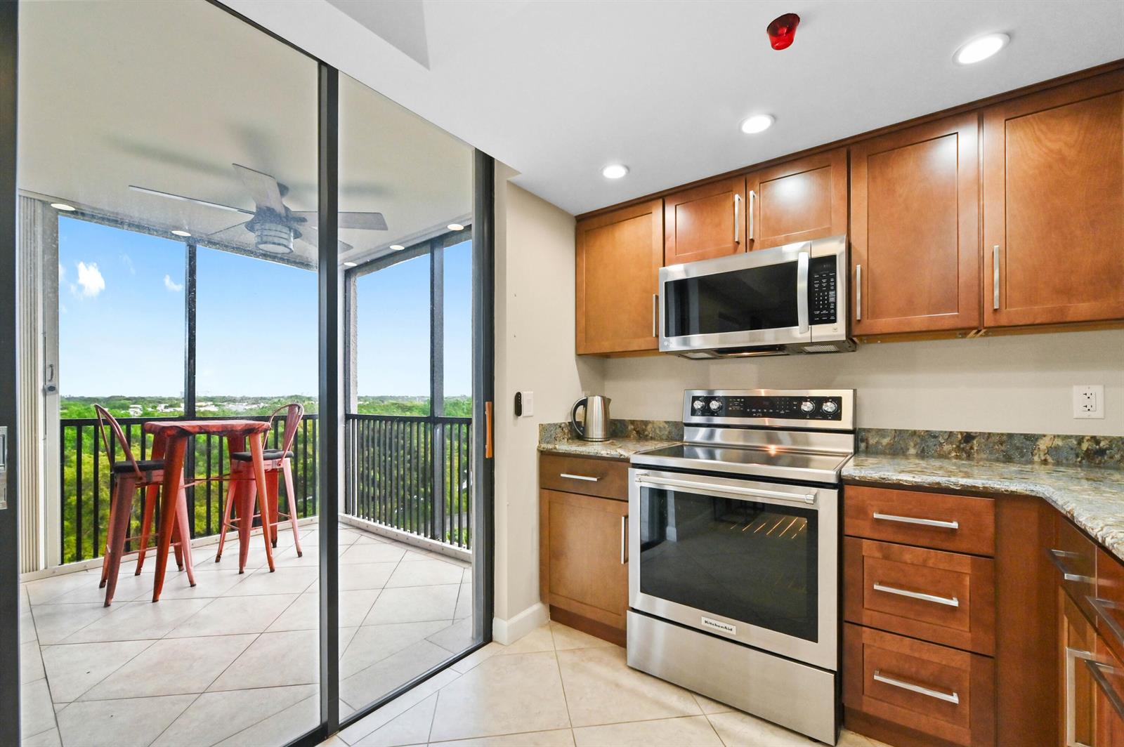 A kitchen with wood cabinets and stainless steel appliances opens onto a screened-in balcony — 5951 Wellesley Park Drive Apt 702, Boca Raton FL 33433, BOCA RATON, FL