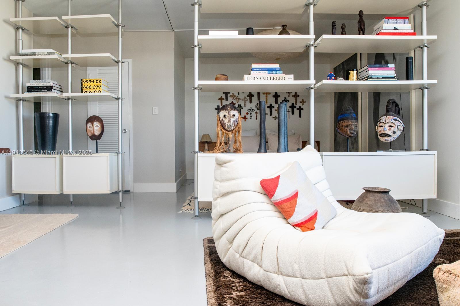 A modern living room features white shelving units, tribal masks, and a white tufted chair — 1000 West Ave # 1504, Miami Beach FL 33139, MIAMI BEACH, FL