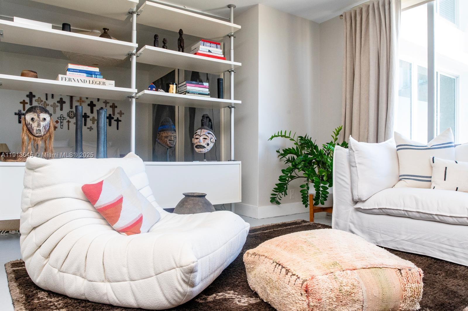A living room features a white tufted chair, a sofa, and shelves displaying decorative masks — 1000 West Ave # 1504, Miami Beach FL 33139, MIAMI BEACH, FL
