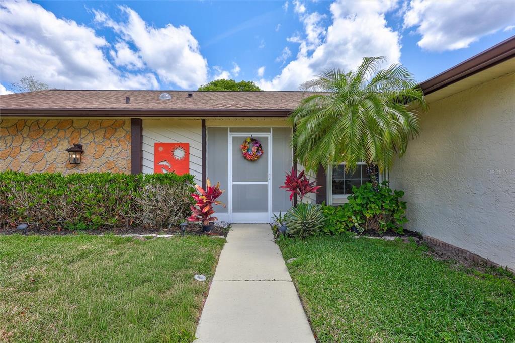 A front exterior view of a house featuring a stone facade, walkway, and palm tree — 1735 ABERDEEN COURT, PALM HARBOR, FL