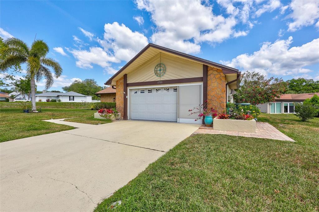 A single-story house features a garage, stone-accented exterior, and a paved driveway under a blue sky — 1735 ABERDEEN COURT, PALM HARBOR, FL